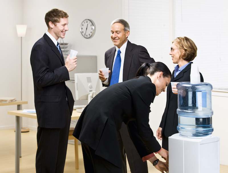 A photo of a group of people gathered around an office water cooler having a conversation