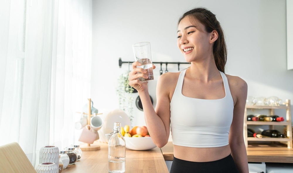 Young woman drinking water after exercising at home