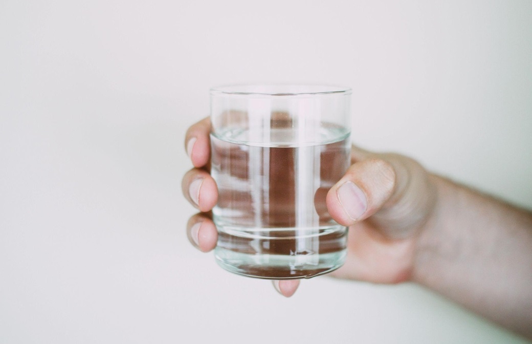 person's hand holding a glass of drinking water